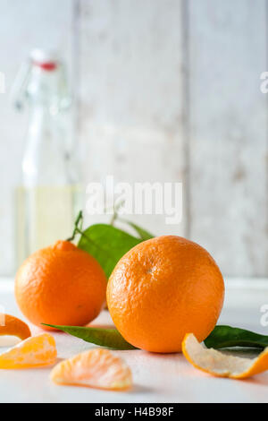 Clementine con fogliame, pezzi di clementine e ciotola di fronte a sfondo luminoso, Foto Stock