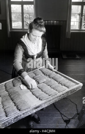 Eine Zigarrenrollerin in Marburger Tracht zählt die fertigen handgerollten Zigarren ab, die auf einem großen Holztablett sortiert sind, bei Marburg, Deutschland 1930er Jahre. Una femmina di sigaro a rulli che indossa un abito di Marburg / costume è il conteggio del finito Foto Stock