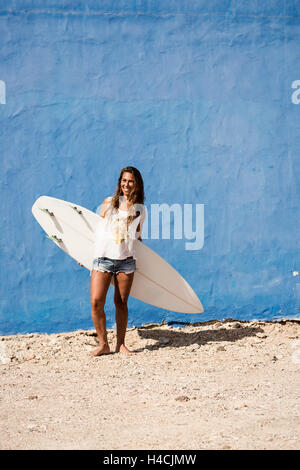 Felice surfer girl con tavola da surf nella parte anteriore della parete di blu Foto Stock