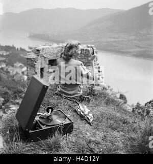 Eine junge Frau sitzt im Gras und hört die neuesten Schlager vom Electrola Koffergrammophon, Deutschland 1930er Jahre. Una giovane donna seduta in un prato e ascoltare le ultime hit da suo grammofono Electrola, Germania 1930s. Foto Stock