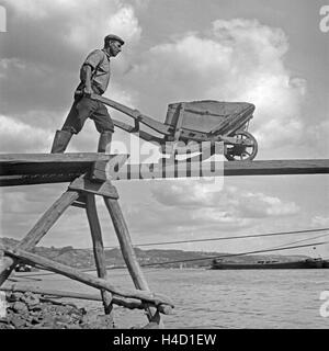 Ein Arbeiter in einem Basaltwerk am Rhein mit circuizione Schubkarre, Deutschland 1930er Jahre. Un lavoratore di un fattore di basalto al fiume Reno con il suo barrow, Germania 1930s. Foto Stock