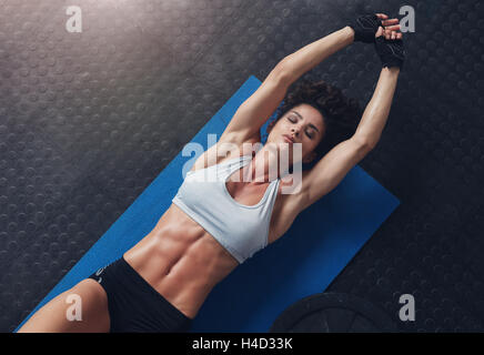 Vista dall'alto della donna sdraiata sul tappeto che fa esercizio di stretching. donna fitness che si allena su un tappetino da yoga in palestra. Foto Stock