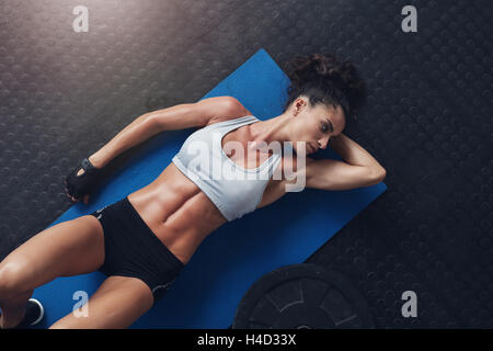 Vista superiore della muscolatura giovane atleta femminile rilassante dopo allenamento. Giovani femmine giacente sul tappeto di esercizi in palestra con la sua mano dietro Foto Stock