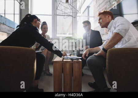 Collega seduto a tavola durante la riunione aziendale. Imprenditori e imprenditrici a discutere di un nuovo progetto in office lob Foto Stock