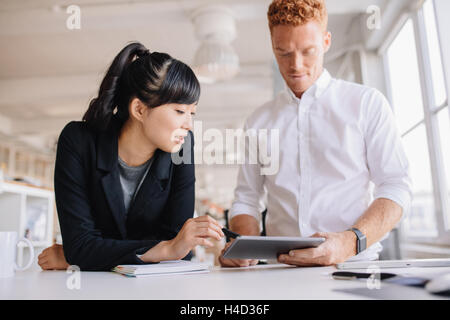 La gente di affari che lavorano insieme su tavoletta digitale in un ufficio moderno. Business l uomo e la donna in piedi alla scrivania guardando tou Foto Stock