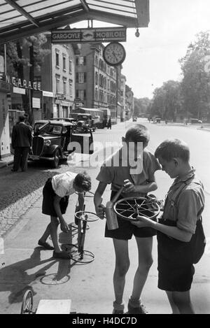 Schuljungen ölen die Räder ihres selbstgebauten Holzwagens un einer Tankstelle, Stoccarda, Deutschland 1930er Jahre. I ragazzi della scuola lubrificando le ruote della loro auto-costruito carrello di legno in corrispondenza di una stazione di benzina, Stuttgart, Germania 1930s. Foto Stock