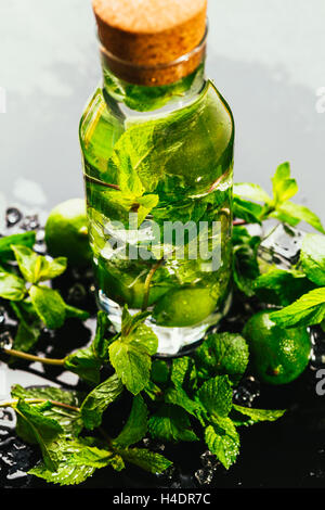 Il mojito bottiglia con lime e menta ice cube close-up su sfondo scuro. Foto Stock