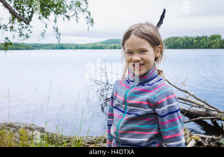 Ragazza con una piuma in capelli sorge sulla riva di un lago e sorrisi nella fotocamera Foto Stock