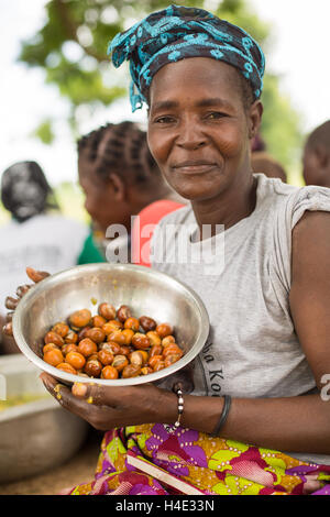 Una donna che tiene una ciotola di appena raccolto noci di karité in nelle zone rurali del dipartimento di Réo, Burkina Faso. Foto Stock