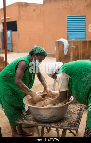 Il lavoro dei dipendenti di varianza manualmente il burro di karité a un commercio equo impianto di produzione in Réo, Burkina Faso. Foto Stock