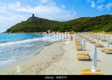 Giovane donna camminando sulla spiaggia con lettini e ombrelloni in Porto Giunco Bay, l'isola di Sardegna, Italia Foto Stock