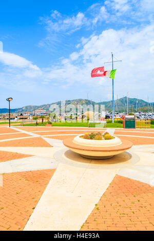 PORTO GIUNCO PORTO, SARDEGNA - 25 Maggio 2014: Piazza con vaso di fiori e bandiera italiana nel Porto Giunco porta. Questo luogo popolare per i turisti di noleggiare barche e fare gite intorno all'isola di Sardegna. Foto Stock