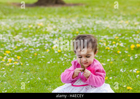 Carino chubby toddler guardando una foglia curiosamente esplorando la natura all'aperto nel parco Foto Stock