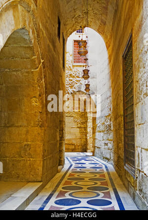 Il stretto corridoio, decorato con le colorate piastrelle di pietra sul pavimento, conduce al cortile di madrasa, Cairo Egitto Foto Stock