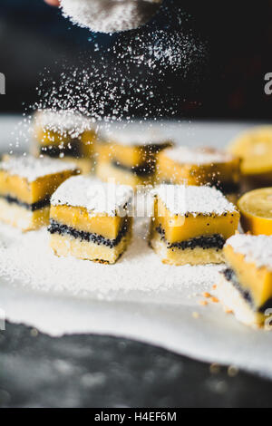 Zucchero di setacciatura su barre di limone o limone piazze i biscotti con semi di papavero Foto Stock