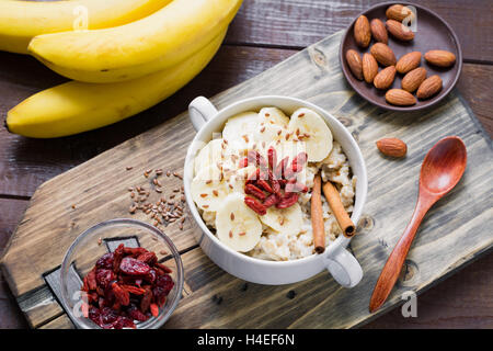 Farina di avena porridge con banana, cannella, secco goji bacche e semi di lino sul tagliere di legno. Cibo sano, uno stile di vita sano Foto Stock