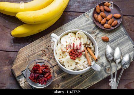 Farina di avena porridge con banana, cannella, secco goji bacche e semi di lino sul tagliere di legno. Cibo sano, uno stile di vita sano Foto Stock
