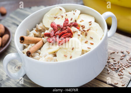 Farina di avena porridge nel recipiente con banana, cannella, secco goji bacche e i semi di lino Foto Stock