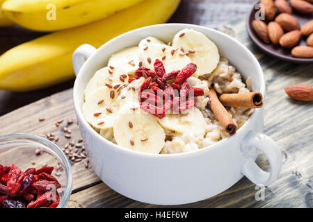 Porridge di fiocchi d'avena con banana, secco goji bacche, semi di lino e cannella. Dieta sana prima colazione Foto Stock