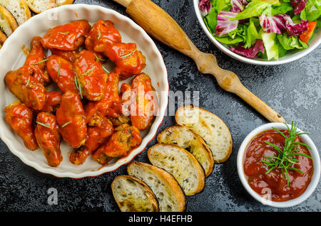 Hot ali di pollo con il piccante salsa habanero e insalata mista con pomodorini e grigliate di baguette con olio d'oliva Foto Stock