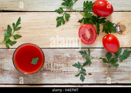 Bicchiere di succo di pomodoro con foglie verdi su uno sfondo di legno, vista dall'alto. Foto Stock
