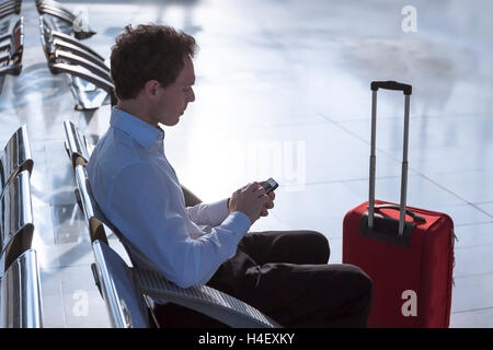 Imprenditore in aeroporto con lo smartphone e valigia controllo messaggi di posta elettronica prima di salire a bordo Foto Stock
