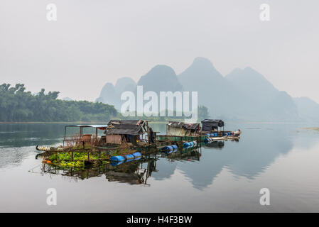 Case e zattera di bambù sul fiume Li isola galleggiante nella cortina di nubi brutto giorno nelle zone rurali di Yangshuo Foto Stock
