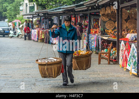 Donna cinese trasporta ceste di produrre e frutta da vendere nel mercato locale di Yangshuo, Cina Foto Stock