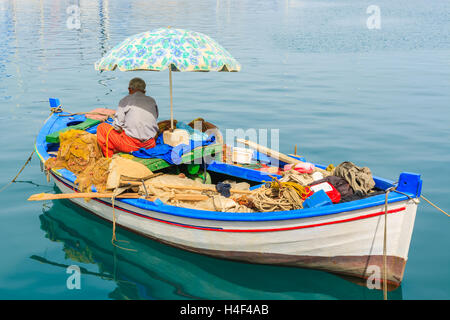 Pescatore seduto sul greco tradizionale barca da pesca e la pulizia di rete da pesca nel porto di Sami village, l'isola di Cefalonia, Grecia Foto Stock