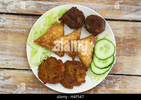 Piatto pieno di spuntini Indiano comprese samosa, cipolla bhajis e pakoras rustico sulla superficie di legno Foto Stock