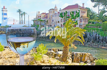 La Scenic Santa Marta faro e la Villa di Santa Maria, sulla Baia rocciosa, si riflettono nel bicchiere di vino bianco, Cascais Foto Stock