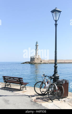 Biciclette appoggiata contro un lampione con il vecchio faro in background, Chania, Creta, Grecia Foto Stock