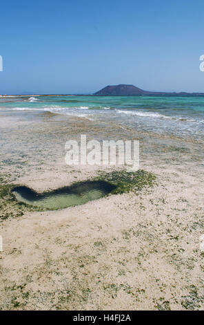 Fuerteventura Isole Canarie, Nord Africa, Spagna: un cuore di roccia a forma durante la bassa marea sulla spiaggia di Grandes Playas con la piccola isola di Lobos Foto Stock