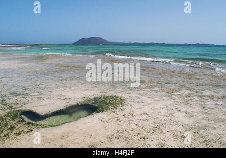 Fuerteventura Isole Canarie, Nord Africa, Spagna: un cuore di roccia a forma durante la bassa marea sulla spiaggia di Grandes Playas con la piccola isola di Lobos Foto Stock