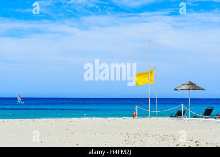Bandiera gialla sulla spiaggia sabbiosa con windsurf sul mare in lontananza, l'isola di Sardegna, Italia Foto Stock