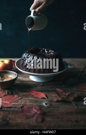 La Carruba e apple bundt torta su un vassoio per dolci e femmina drizzling mano ganache al cioccolato Foto Stock