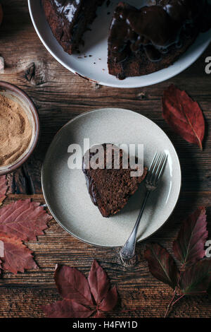 La Carruba e apple bundt cake con glassa al cioccolato su un cavalletto di torta e una fetta di torta sul piatto da dessert Foto Stock