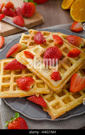 Waffles fatti in casa con lo sciroppo di acero e fragole, ricoperto di crema e scaglie di cioccolato, arancione bevanda fresca Foto Stock