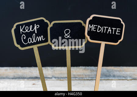 Mantenere la calma e a meditare messaggio scritto con un gessetto sulla lavagna mini etichette, lavagna sfocati e tavolo in legno in background. Divertimento e umorismo concept Foto Stock