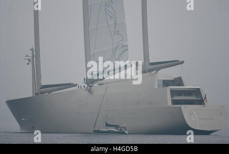 Strande, Germania. Xvi oct, 2016. A 13 metri di lunghezza della nave a vela del tipo Beneteau Oceanis 43 aziona passato il più grande yacht a vela in tutto il mondo, "Yacht UN', sul quale un equipaggio è pronta a salpare sull'albero maestro, nella nebbia fiordo di Kiel in Strande, Germania, 16 ottobre 2016. Il gigante yacht è sull'acqua per il primo test di navigazione a vela. Foto: Axel HEIMKEN/dpa/Alamy Live News Foto Stock