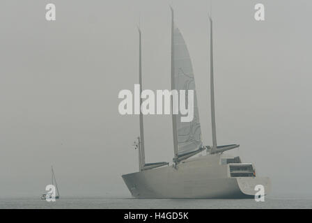 Strande, Germania. Xvi oct, 2016. A 13 metri di lunghezza della nave a vela del tipo Beneteau Oceanis 43 aziona passato il più grande yacht a vela in tutto il mondo, "Yacht UN', sul quale un equipaggio è pronta a salpare sull'albero maestro, nella nebbia fiordo di Kiel in Strande, Germania, 16 ottobre 2016. Il gigante yacht è sull'acqua per il primo test di navigazione a vela. Foto: Axel HEIMKEN/dpa/Alamy Live News Foto Stock