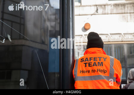 IPhone 7 Pubblicità in Manchester Piccadilly con uomo che indossa ' qui per aiutare' hi-vis Team Sicurezza camicia, REGNO UNITO Foto Stock