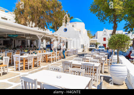 La città di Mykonos, Grecia - 16 Maggio 2016: Greco gli uomini che parlano in taverna tipica con sedie e tavoli di fronte ad una chiesa bianca nel mio Foto Stock