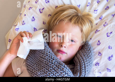Ammalati bambino ragazzo soffia il naso che stabilisce nel letto con la faccia triste - Salute e medicina concept Foto Stock