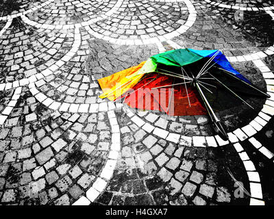 Ombrello rotto nei colori dell'arcobaleno dopo una pioggia pesante disteso sul marciapiede fatta di ciottoli Foto Stock