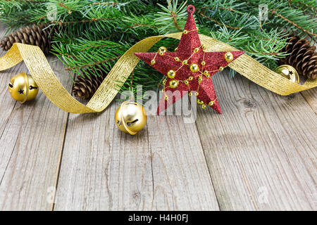 Stella Rossa con ornamento d'oro, Natale Jingle Bells e nastri su weathered tagliere in legno Foto Stock