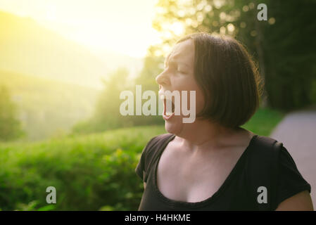 Giovane donna adulta sbadigli all'aperto al mattino, assonnato stanco persona di sesso femminile a piedi nella natura Foto Stock