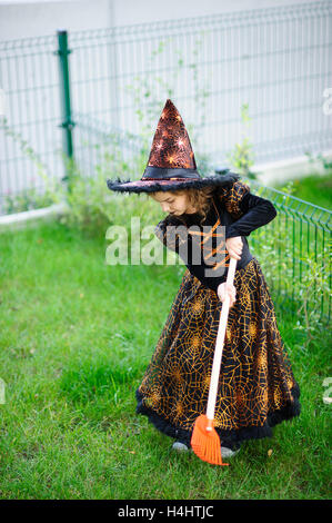 Preparazione per la festa di Halloween. La ragazza in un abito della strega malvagia pulisce un prato di rastrello. La ragazza è vestita di un nero-arancio di dre Foto Stock