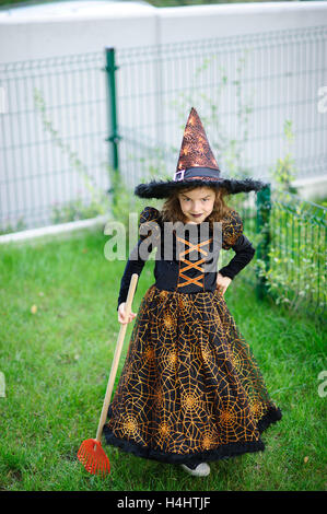 Preparazione per la festa di Halloween. La ragazza in un abito della strega malvagia pulisce un prato di rastrello. La ragazza è vestita di un nero-arancio di dre Foto Stock