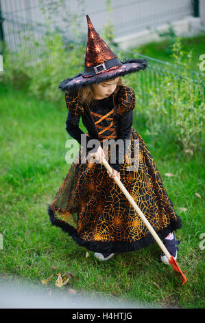 Preparazione per la festa di Halloween. La ragazza in un abito della strega malvagia pulisce un prato di rastrello. La ragazza è vestita di un nero-arancio di dre Foto Stock